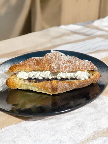 アンホイップクロワッサン with whipped cream and sweetened red bean filling, dusted with powdered sugar on a black plate.