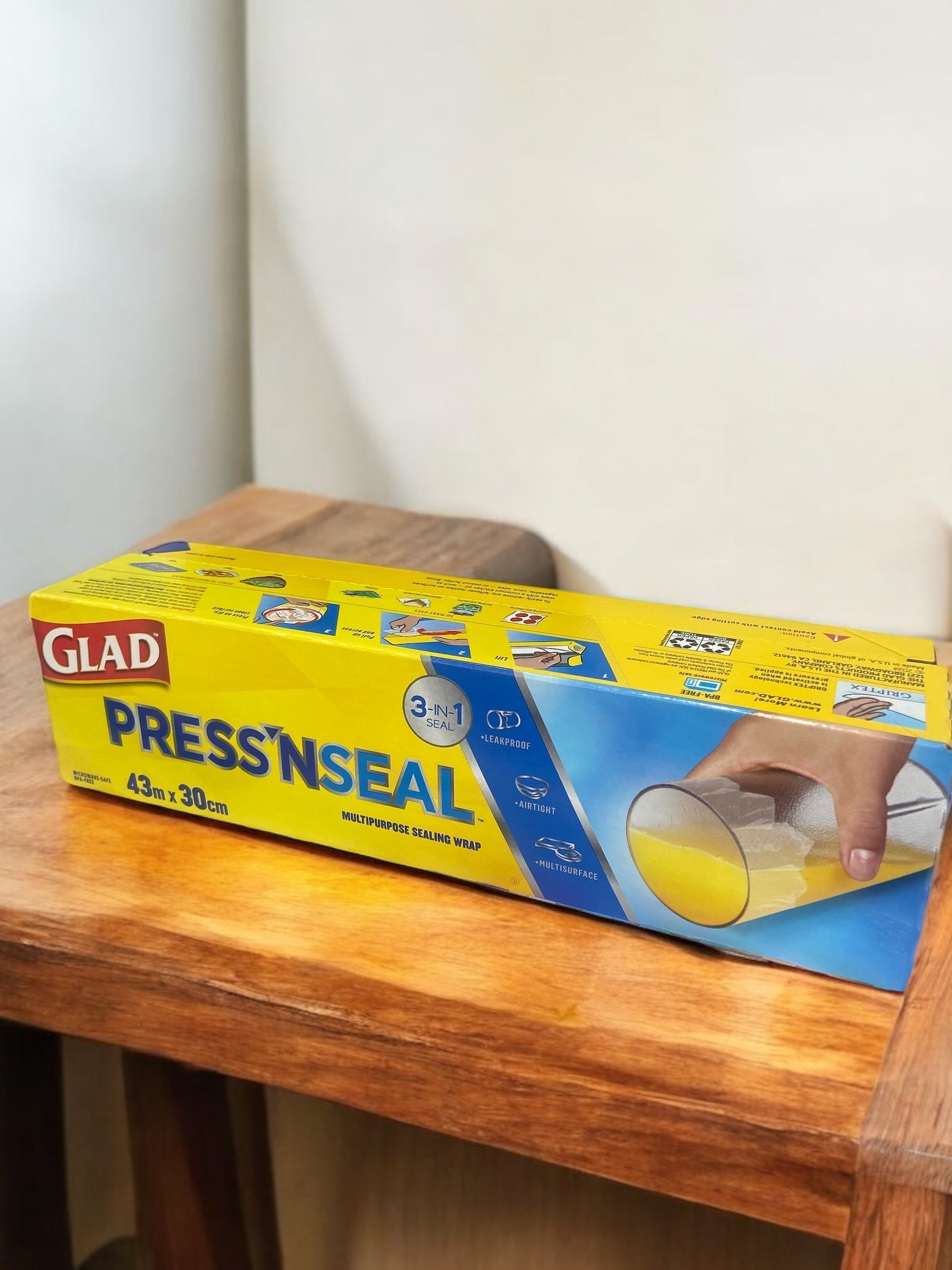 GLAD Press'n Seal storage wrap on a wooden table, showcasing vacuum sealing and griptex technology for fresh food storage.