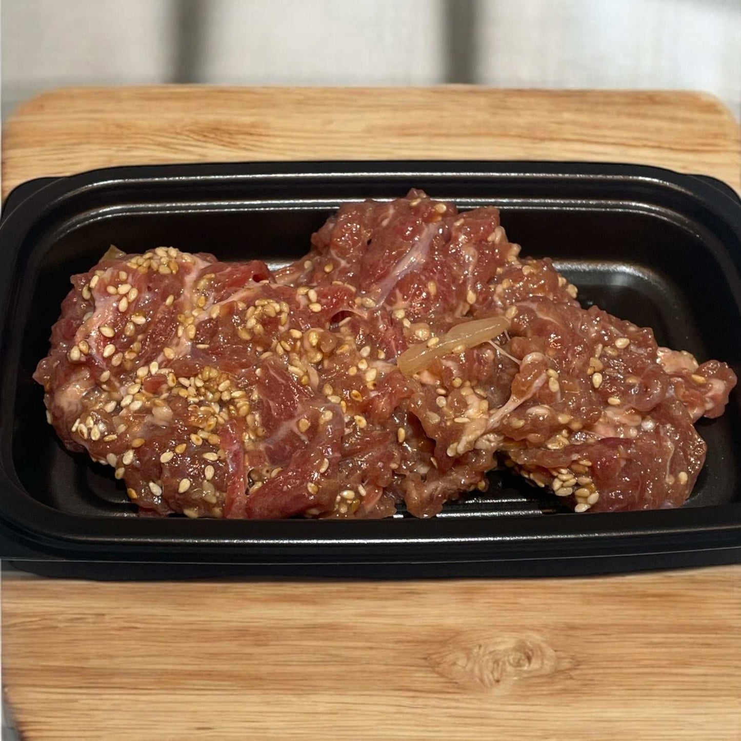 150g pack of marinated bulgogi beef with sesame seeds in black tray on wooden surface