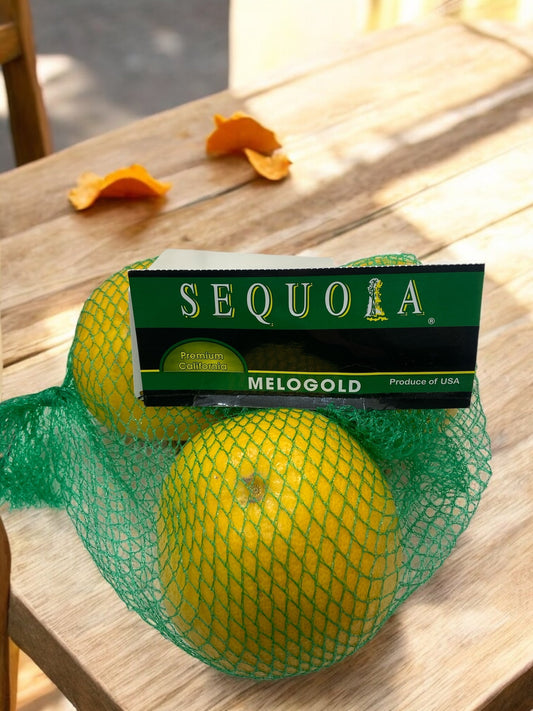 Seasonal Melogold fruit set with three large grapefruits in green mesh packaging on wooden table.